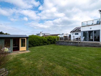 A backyard with a wooden deck attached to a house and a small shed on a lawn at Lowenda in Polzeath
