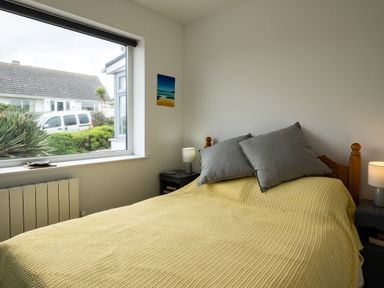 A bedroom with a yellow bedspread gray pillows and a window showing a white van and bushes at Lowenda in Polzeath