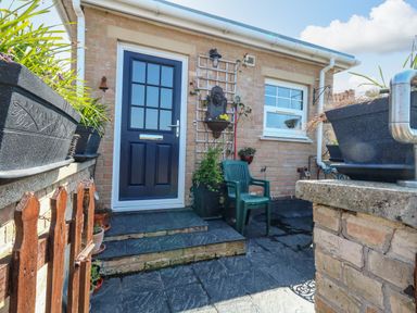 An outdoor patio area with a black door, green plastic chair, potted plants, and brick walls at Beach Retreat in Weymouth