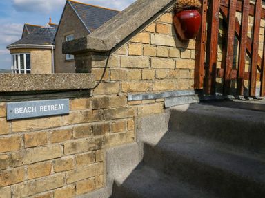 A brick wall with a sign that says Beach Retreat and concrete steps leading up to a wooden gate at Beach Retreat in Weymouth