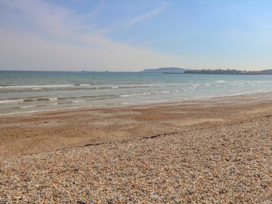 A pebble and sandy beach with small waves and distant land on the horizon at Beach Retreat in Weymouth