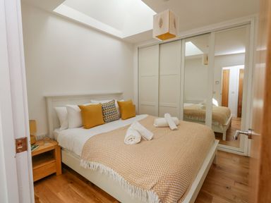 A bedroom with a bed with pillows and rolled towels a bedside table and a wardrobe with mirrored sliding doors at Beach Retreat in Weymouth