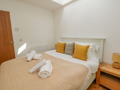 A bedroom with a bed with white linens and yellow pillows and a wooden nightstand with a lamp a glass and a wooden door at Beach Retreat in Weymouth