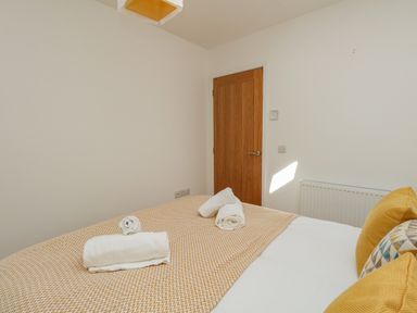 A bedroom with a bed covered with a yellow patterned blanket and rolled white towels on Beach Retreat in Weymouth