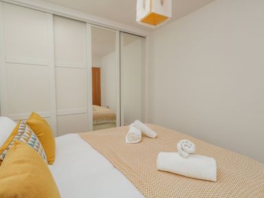 A bedroom with a bed covered with a patterned duvet and folded towels and sliding mirrored wardrobe doors at Beach Retreat in Weymouth