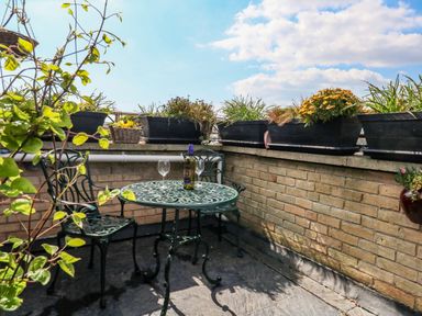 A small outdoor patio with a round metal table and two chairs with plants in pots on a brick wall at Beach Retreat in Weymouth