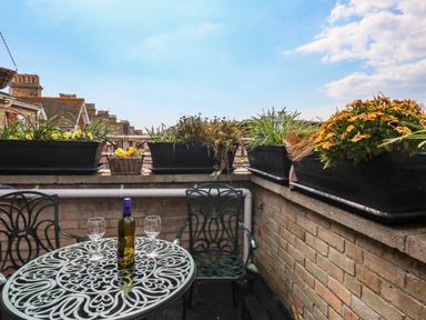 A balcony with a metal table and two chairs with a bottle and two glasses on the table at Beach Retreat in Weymouth