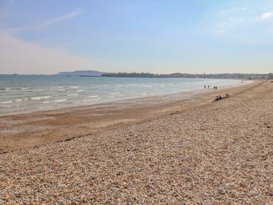 A pebble beach with people walking and sitting near the water at Beach Retreat in Weymouth