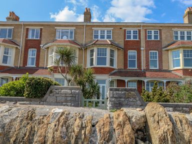 A row of brick townhouses with bay windows and small front gardens behind a stone wall at Beach Retreat in Weymouth