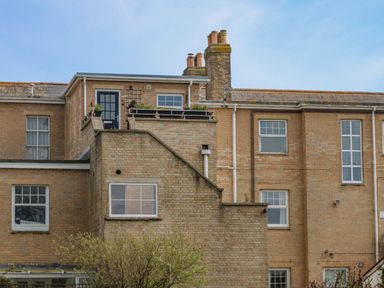 The back of a brick building with multiple windows a small balcony with plants and a door at Beach Retreat in Weymouth