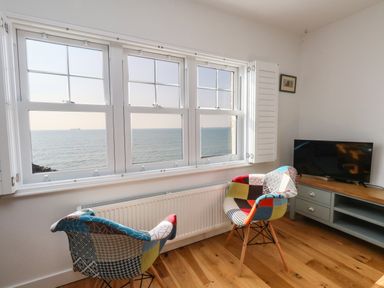A room with two multicolored chairs facing windows overlooking the sea and a TV on a wooden cabinet at Beach Retreat in Weymouth
