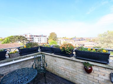 A balcony with metal table and chairs and flower pots on the ledge at Beach Retreat in Weymouth