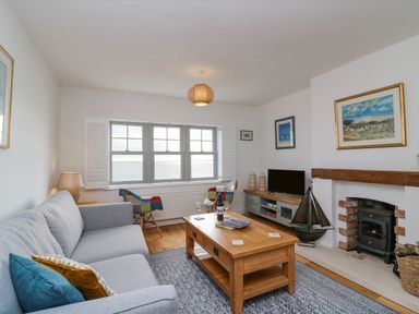 A living room with a blue sofa a wooden coffee table a wood burning stove and windows showing a sea view at Beach Retreat in Weymouth