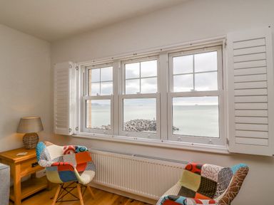 A room with two patchwork chairs a wooden side table with a lamp and a window overlooking the sea at Beach Retreat in Weymouth