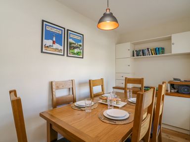 A dining room with a wooden table and six chairs set with plates glasses and cupcakes with framed pictures on the wall and shelves with books and a radio at Beach Retreat in Weymouth