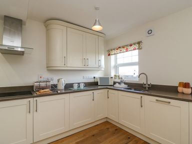 A kitchen with cream cabinets a toaster a kettle a microwave and a window with a floral blind at Beach Retreat in Weymouth