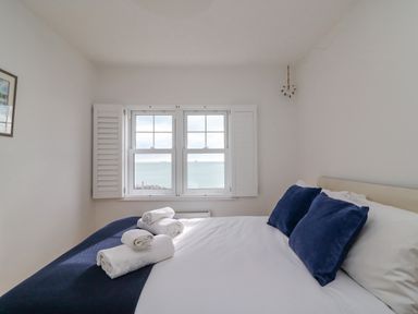 A bedroom with a bed made with white linens and blue pillows facing a window with a sea view at Beach Retreat in Weymouth