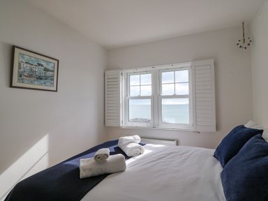 A bedroom with a bed and rolled towels by a window showing a sea view at Beach Retreat in Weymouth