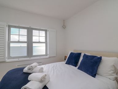 A bedroom with a bed with white sheets and blue pillows next to a window with a sea view at Beach Retreat in Weymouth