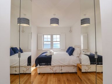 A bedroom with a bed blue pillows a window with shutters and wooden floor at Beach Retreat in Weymouth