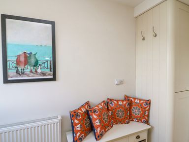 A corner of a room with a bench and four patterned cushions below a framed painting and two wall hooks at Beach Retreat in Weymouth