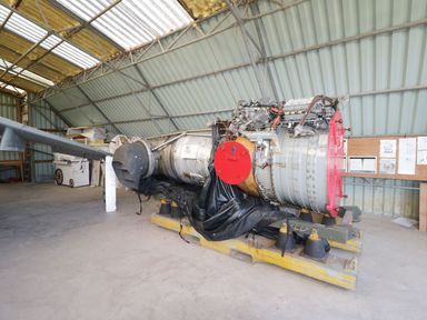 A large aircraft engine inside a metal shed with notes on a wooden board at Owl Lodge in Wedmore