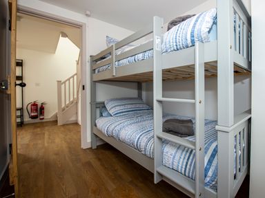 A bedroom with a grey bunk bed and blue striped bedding and a doorway leading to a hallway with stairs and fire extinguishers at Owl Lodge in Wedmore
