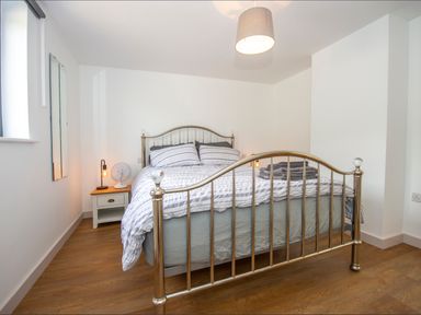 A bedroom with a metal bed frame a bedside table with a lamp and fan and folded towels on the bed at Owl Lodge in Wedmore
