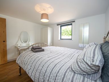A bedroom with a bed with striped bedding a white dressing table a white wardrobe and a window at Owl Lodge in Wedmore