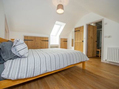 A bedroom with a wooden bed and striped bedding a skylight and wooden doors at Owl Lodge in Wedmore