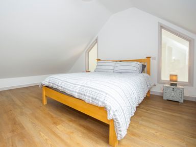 A bedroom with a wooden bed frame and striped bedding on a wooden floor at Owl Lodge in Wedmore