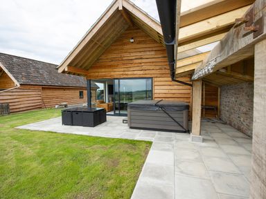 A patio area with a hot tub and outdoor seating next to a wooden building at Owl Lodge in Wedmore