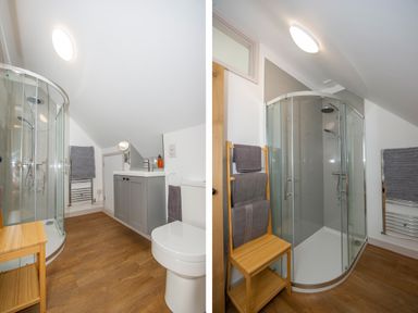 A bathroom with a curved glass shower enclosure a toilet a sink with a cabinet a wooden towel rack with towels and wooden flooring at Owl Lodge in Wedmore