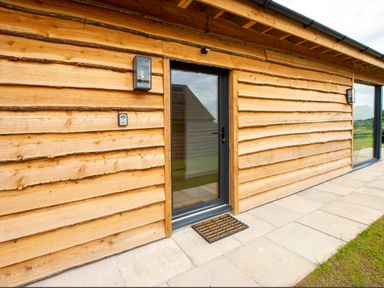 A wooden exterior wall with a glass door and two wall lights at Starling Lodge in Wedmore