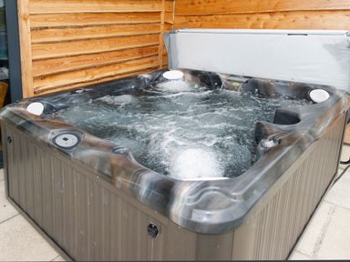 An outdoor hot tub with bubbling water next to a wooden wall at Starling Lodge in Wedmore