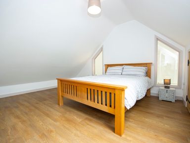 A bedroom with a wooden bed and striped bedding beside two triangular windows and a small bedside table with a lamp at Starling Lodge in Wedmore