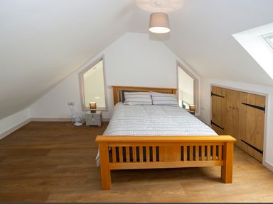 A bedroom with a wooden bed frame a bed with striped bedding two bedside tables with lamps and a small fan on the floor at Starling Lodge in Wedmore