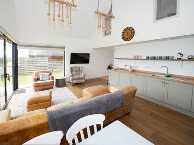 A living room with leather and fabric armchairs a wall clock and kitchen cabinets at Starling Lodge in Wedmore