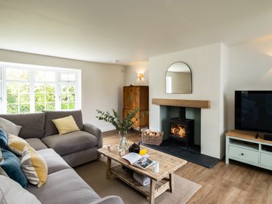 A living room with a grey sofa, wooden coffee table, fireplace with fire, TV, and wooden cabinet at Samphire Rock