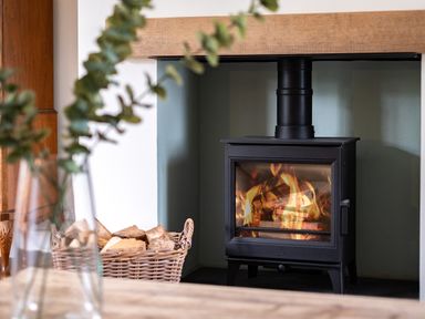 A wood burning stove with fire inside and a basket of firewood beside it at Samphire in Rock