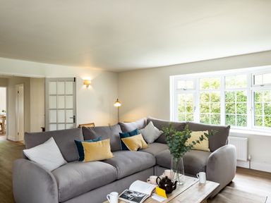 A living room with a large grey sectional sofa with cushions and a wooden coffee table with a teapot and an open book at Samphire in Rock