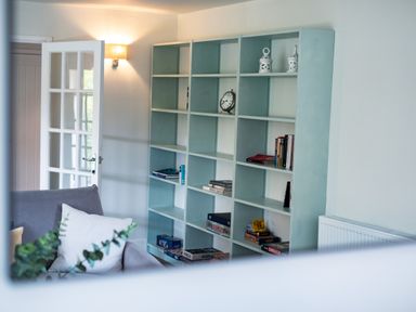 A living room with a bookshelf filled with books and games and a gray armchair with cushions at Samphire in Rock