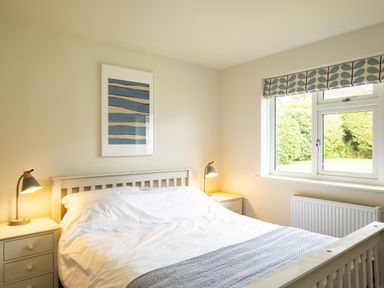 A bedroom with a double bed white bed frame two bedside tables with lamps a window and a framed picture on the wall at Samphire in Rock