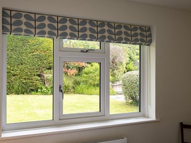 A window with a patterned valance overlooking a garden with bushes and grass at Samphire in Rock