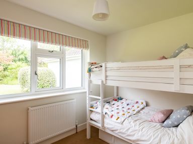 A bedroom with a white bunk bed next to a window and a radiator at Samphire in Rock