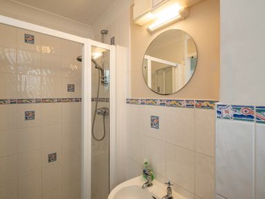 A bathroom with a shower enclosure a sink a round mirror and decorative tiled walls at Samphire in Rock