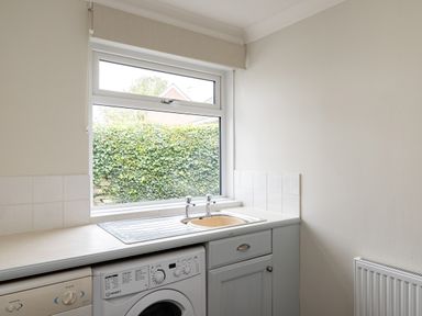 A kitchen area with a window above a sink a washing machine and a dishwasher at Samphire in Rock