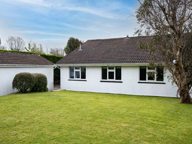 A lawn area with a white house and a small building with tiled roofs and some bushes and a tree at Samphire in Rock