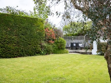 A garden with a lawn, trees, shrubs, and an outdoor dining table with chairs at Samphire in Rock