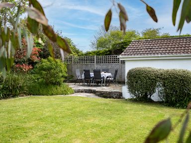 A garden with a lawn a stone patio set with table and chairs and a white building with a tiled roof at Samphire Rock